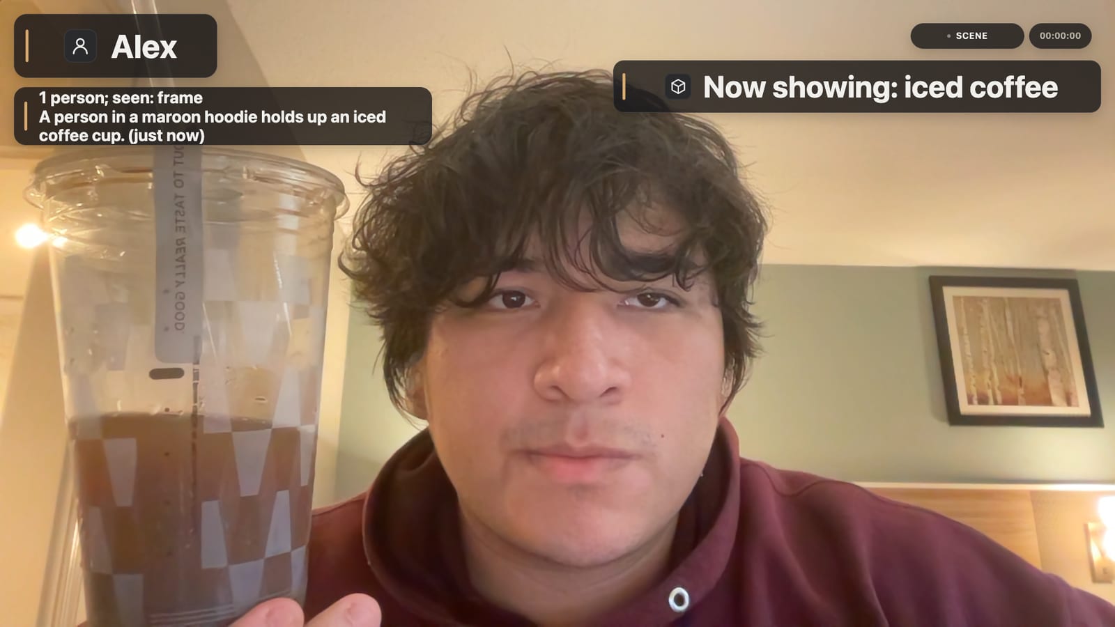Alex holds up an iced coffee. Sceneuron shows “Now showing: iced coffee” and a live description: “A person in a maroon hoodie holds up a plastic cup of iced coffee.”